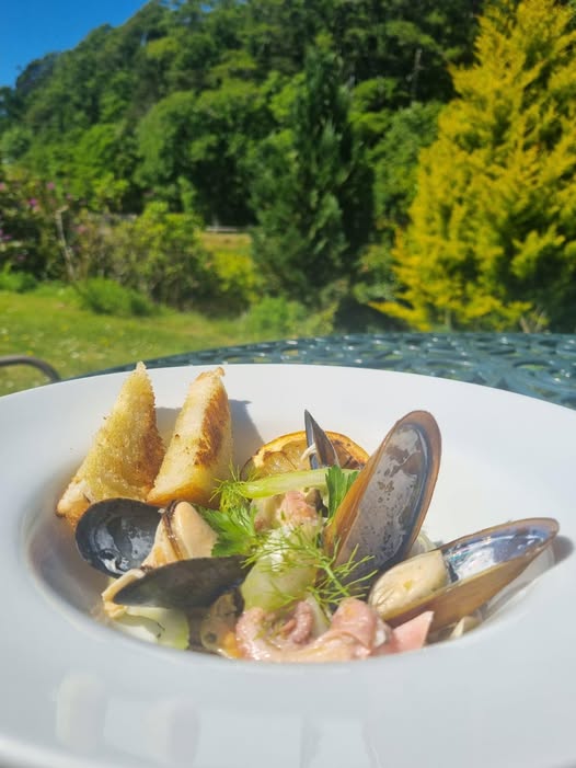 A bowl of fresh steamed mussels and toasted garlic bread served outdoors at our Gairloch restaurant, overlooking the greenery of Flowerdale Glen.