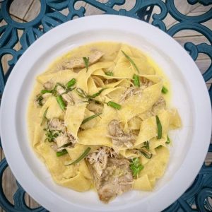 A plate of creamy pappardelle pasta with pulled chicken and fresh greens, served on the outdoor terrace at The Old Inn.