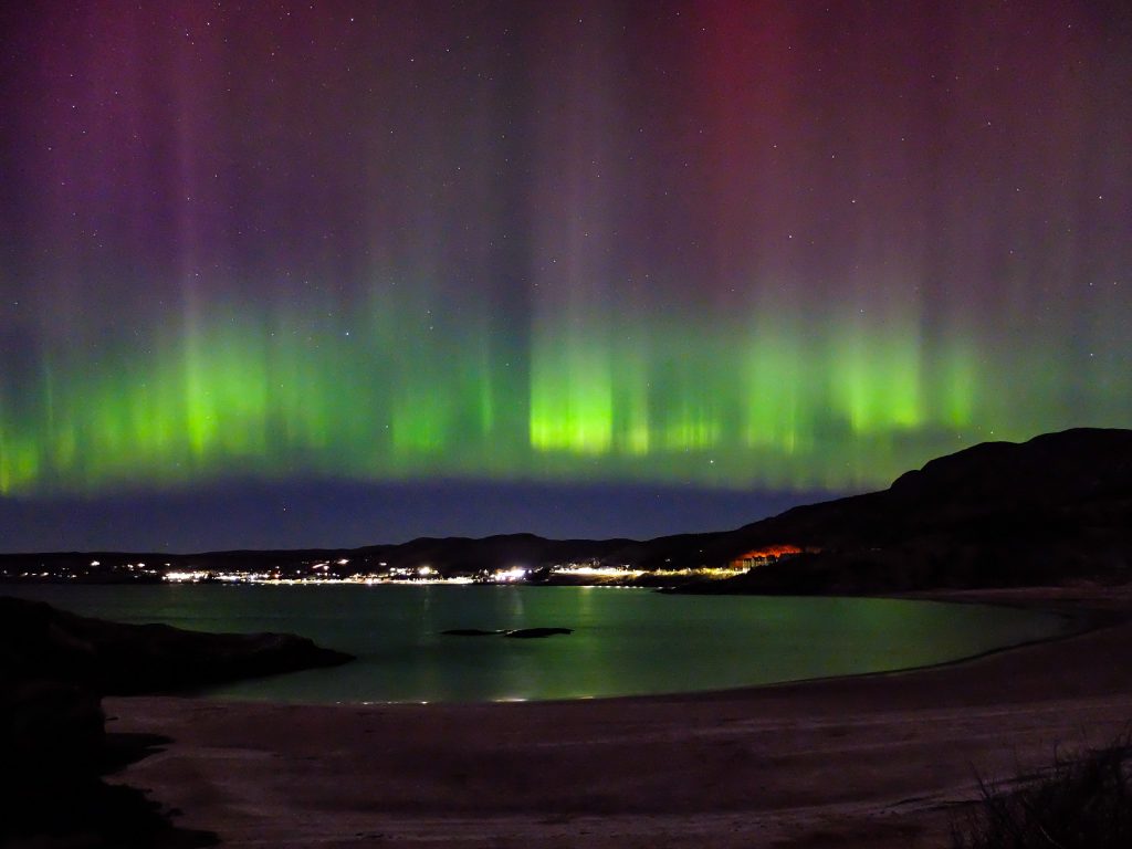 The Aurora Borealis (Northern Lights) glowing green and purple over Gairloch bay, a breathtaking sight for visitors staying in our NC500 accommodation.