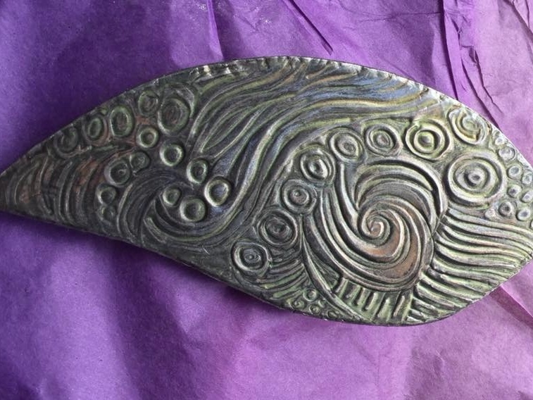 A detailed embossed pewter brooch with Celtic-inspired imagery, handcrafted during a creative workshop at The Old Inn.