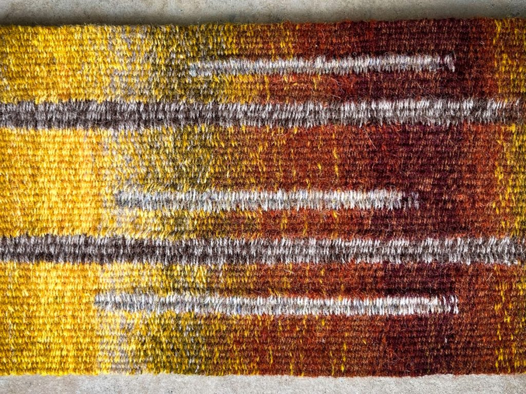 Hands carefully working on a traditional hand-weaving loom using colourful woollen yarns during a Highland craft workshop.