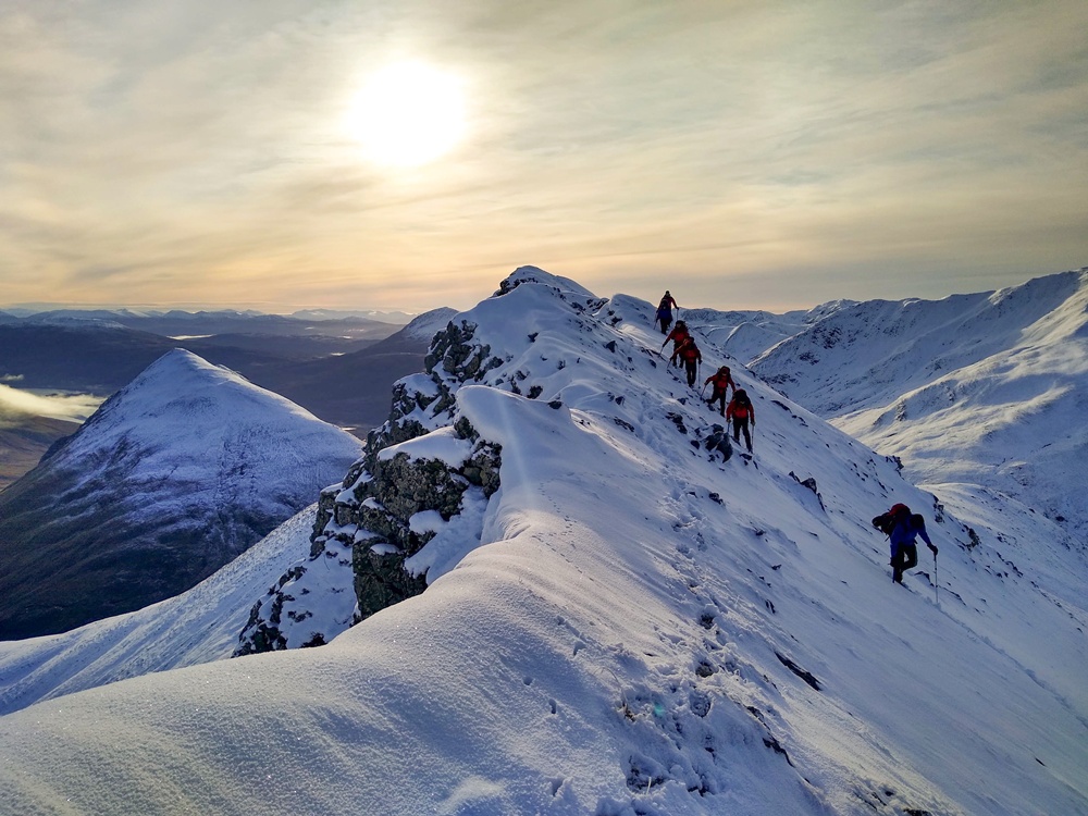 A mountain guide leading hikers across a snow-covered Highland ridge, a highlight of winter mountaineering courses in Gairloch.