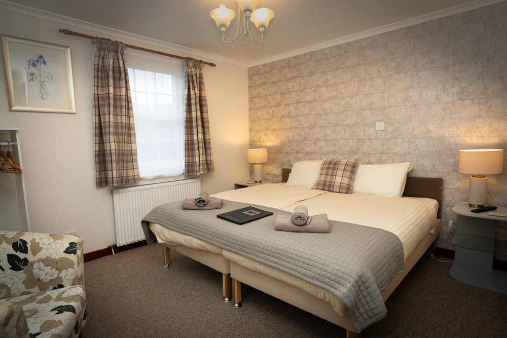Traditional guestroom at The Old Inn Gairloch featuring tartan cushions, neutral decor, and a cosy double bed for a classic Highland stay.