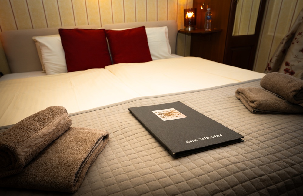 Guestroom at The Old Inn Gairloch featuring a large bed with red cushions, fresh towels and guest information in a traditional Highland inn.