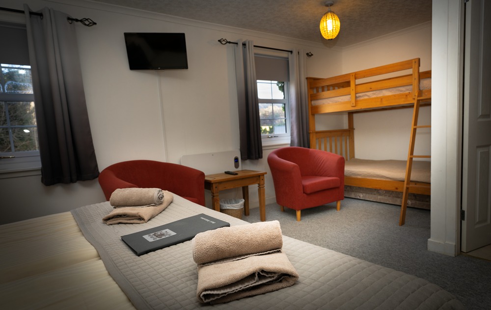 Family-friendly guestroom at The Old Inn Gairloch featuring wooden bunk beds, a large double bed, and red armchairs for a comfortable NC500 family stay.